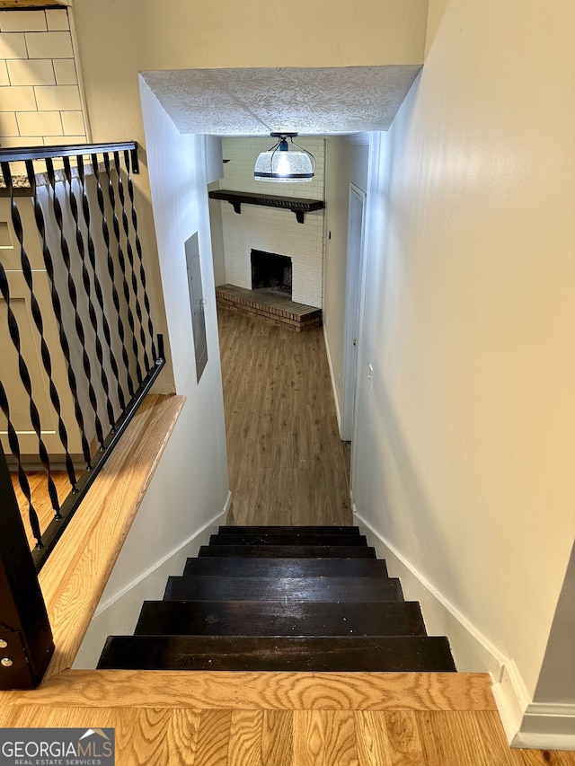 stairs with wood-type flooring, electric panel, a brick fireplace, and a textured ceiling