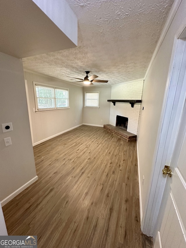 unfurnished living room featuring ornamental molding, a textured ceiling, a brick fireplace, ceiling fan, and hardwood / wood-style flooring