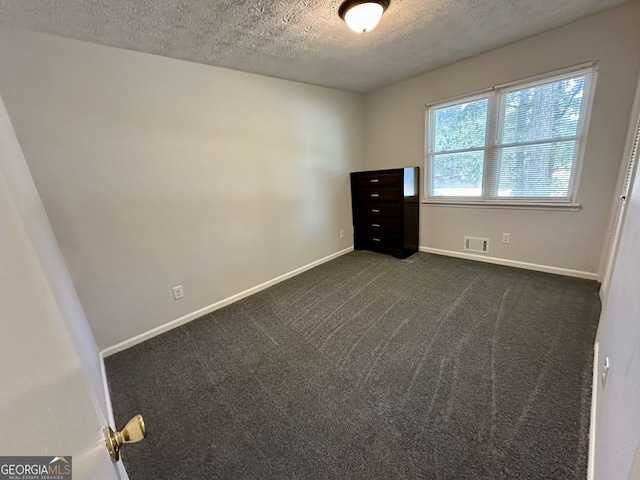 empty room with a textured ceiling and dark colored carpet