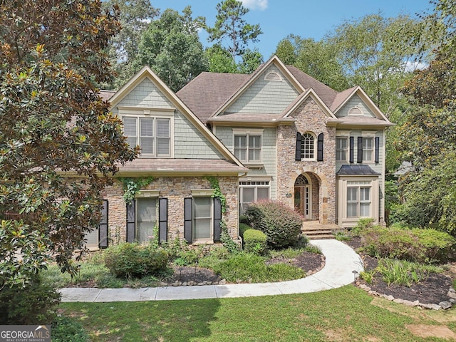 view of front of home featuring stone siding, a front lawn, and roof with shingles