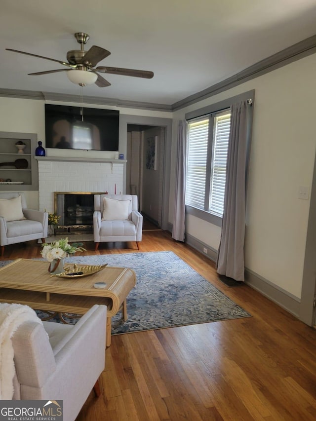 living room featuring hardwood / wood-style floors, ceiling fan, ornamental molding, and a brick fireplace