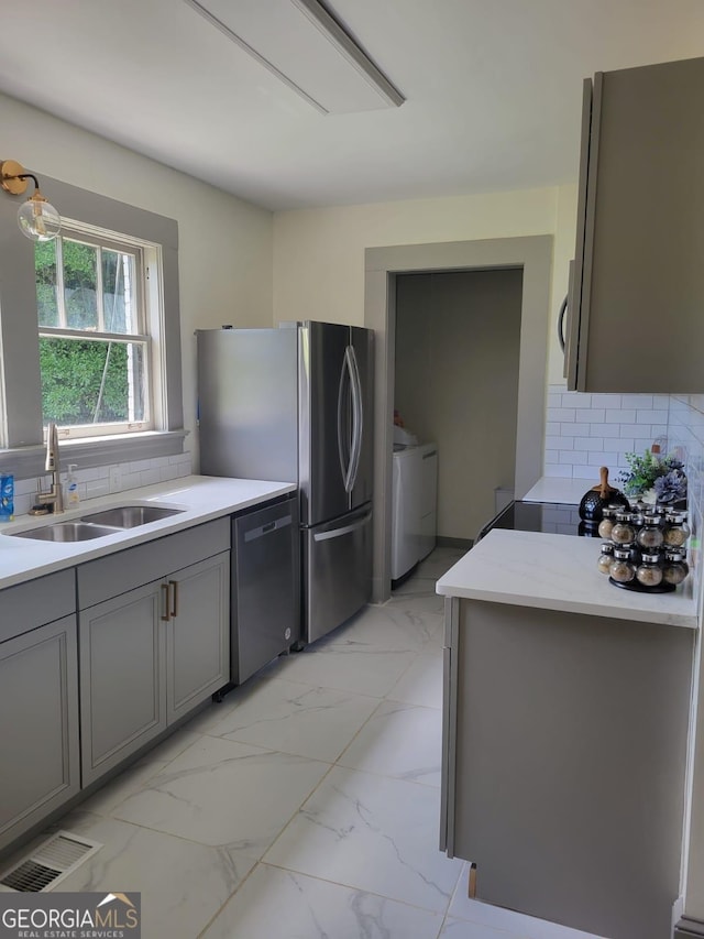 kitchen with sink, decorative backsplash, gray cabinets, independent washer and dryer, and appliances with stainless steel finishes