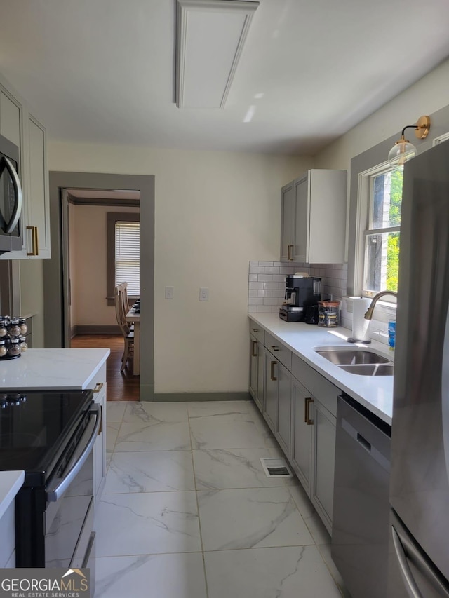 kitchen featuring decorative backsplash, appliances with stainless steel finishes, gray cabinetry, and sink