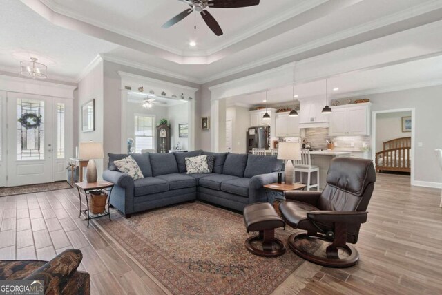 living room featuring crown molding, light hardwood / wood-style floors, ceiling fan, and a raised ceiling