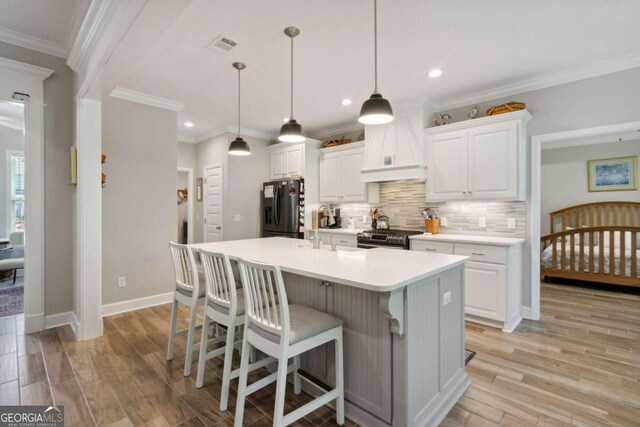 kitchen featuring light wood-type flooring, stainless steel appliances, a kitchen island with sink, tasteful backsplash, and custom exhaust hood