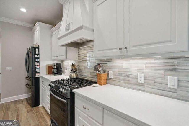 kitchen featuring black range with gas cooktop, custom range hood, tasteful backsplash, refrigerator, and white cabinets