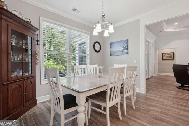 dining room featuring a notable chandelier, ornamental molding, a tray ceiling, and light wood-type flooring