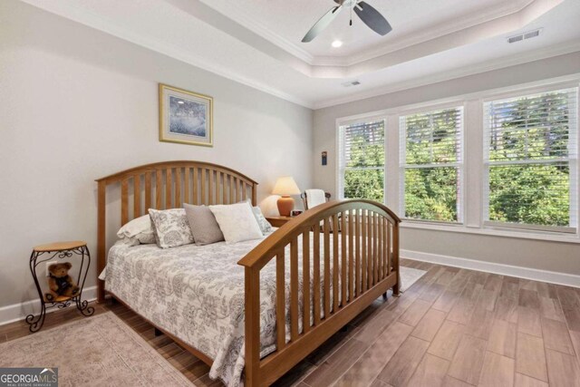 bedroom with ceiling fan, hardwood / wood-style floors, multiple windows, and a raised ceiling