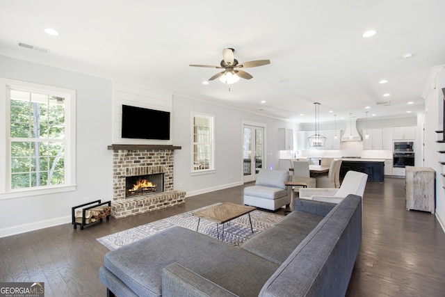 living room featuring ceiling fan, a fireplace, dark wood-type flooring, and ornamental molding