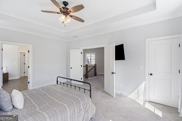 bedroom with light colored carpet, ceiling fan, and a tray ceiling