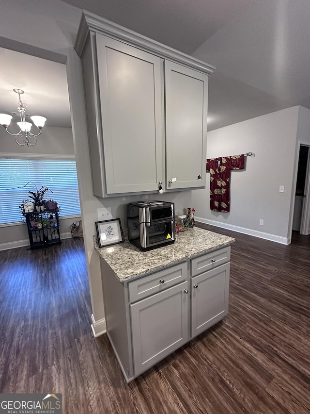 kitchen with gray cabinets, light stone countertops, dark wood-type flooring, and an inviting chandelier