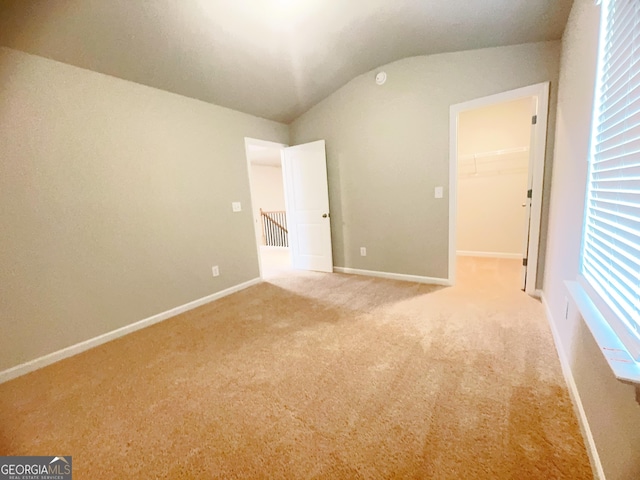 unfurnished bedroom featuring a spacious closet, lofted ceiling, carpet floors, and a closet