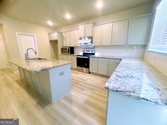 kitchen featuring light stone countertops, appliances with stainless steel finishes, a kitchen island with sink, sink, and light hardwood / wood-style floors