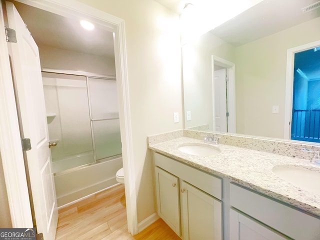 full bathroom featuring hardwood / wood-style flooring, vanity, toilet, and bath / shower combo with glass door