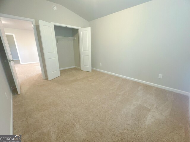 unfurnished bedroom featuring vaulted ceiling, light carpet, and a closet