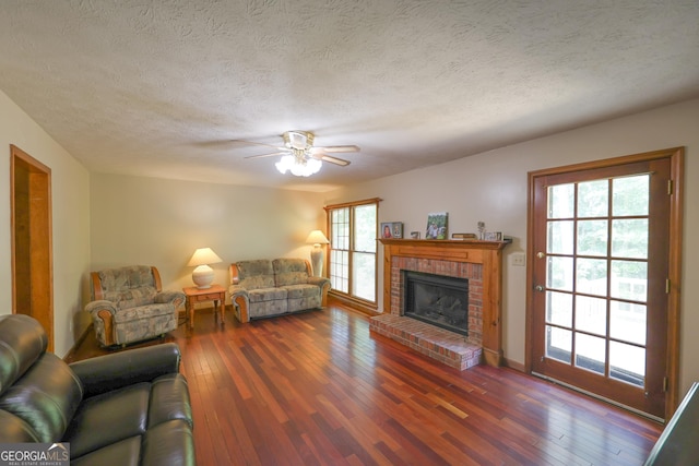 living room with a textured ceiling, dark hardwood / wood-style flooring, a brick fireplace, and ceiling fan