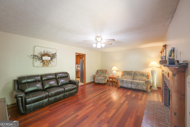 living room featuring a textured ceiling, ceiling fan, dark hardwood / wood-style floors, and a brick fireplace