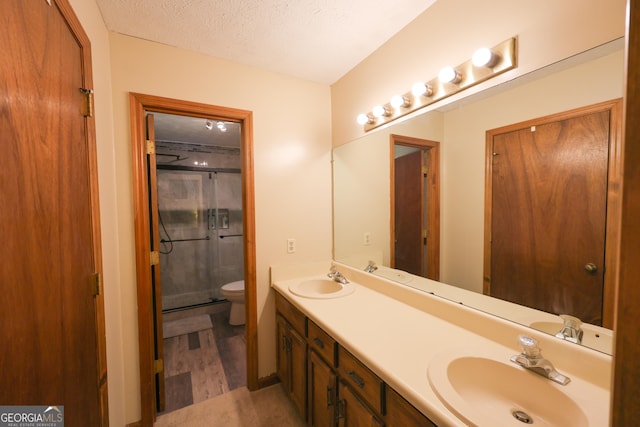 bathroom with hardwood / wood-style floors, a textured ceiling, toilet, a shower with door, and vanity