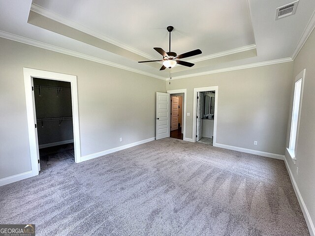 unfurnished bedroom with ceiling fan, crown molding, carpet flooring, and a walk in closet