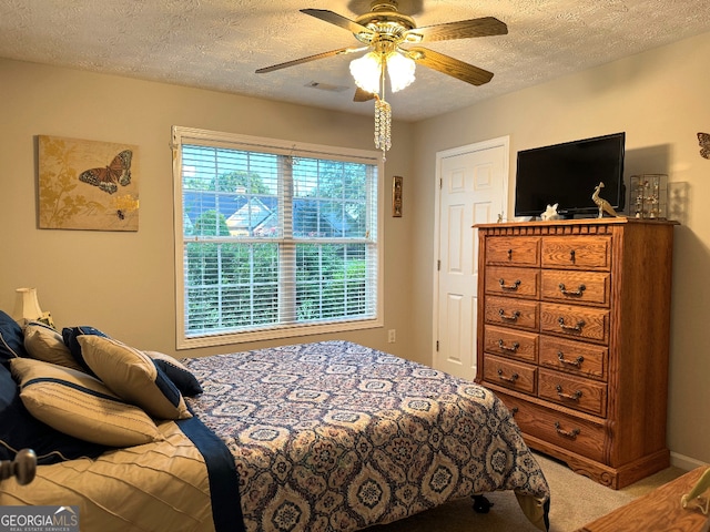 carpeted bedroom featuring ceiling fan and a textured ceiling