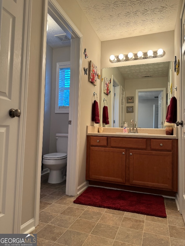 bathroom with tile floors, a textured ceiling, vanity, and toilet