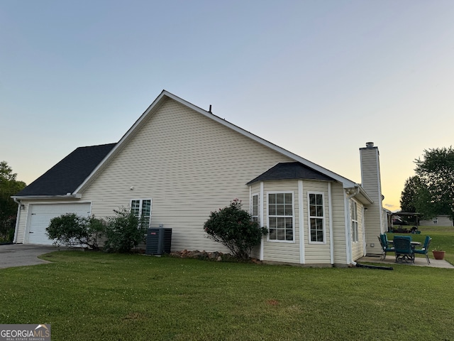 property exterior at dusk with a garage, central AC, and a lawn