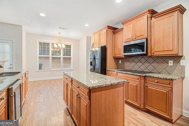 kitchen with pendant lighting, sink, a center island, black appliances, and light wood-type flooring