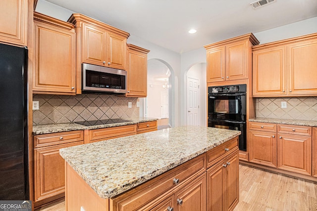 kitchen featuring light stone counters, black appliances, light hardwood / wood-style floors, and a kitchen island