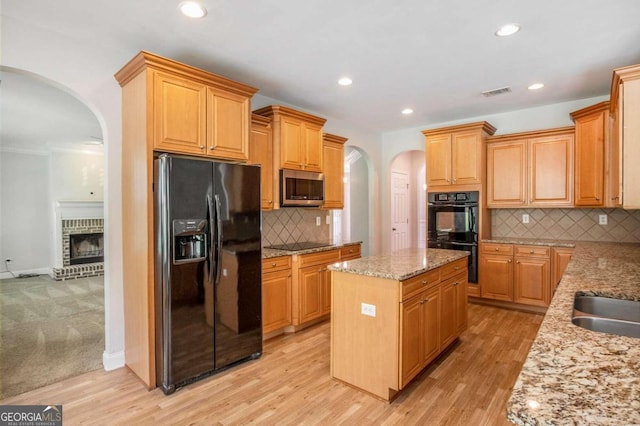 kitchen with a brick fireplace, light hardwood / wood-style flooring, decorative backsplash, a kitchen island, and black appliances