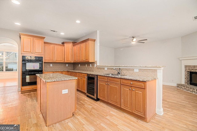 kitchen with wine cooler, light stone counters, double oven, and a kitchen island