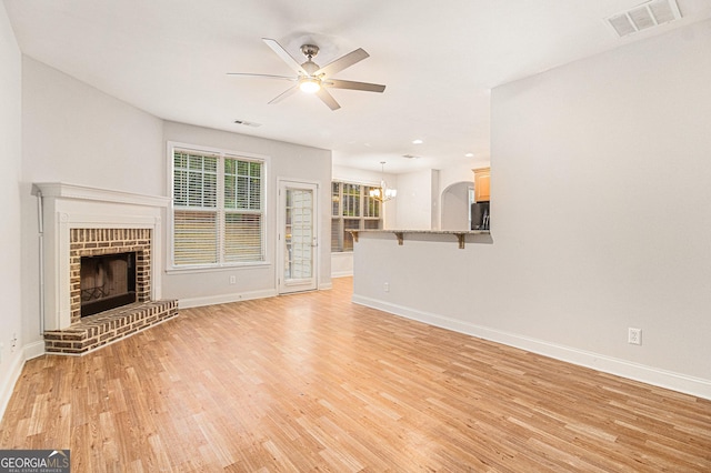 unfurnished living room with a brick fireplace, ceiling fan with notable chandelier, and light wood-type flooring