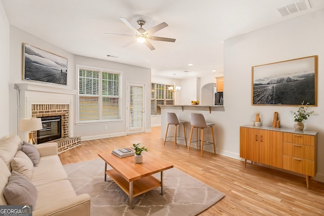 living room with a brick fireplace, ceiling fan with notable chandelier, and light hardwood / wood-style flooring