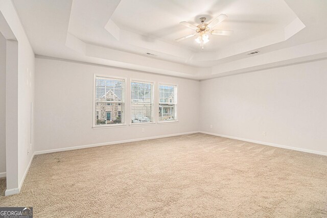 carpeted spare room with a tray ceiling and ceiling fan