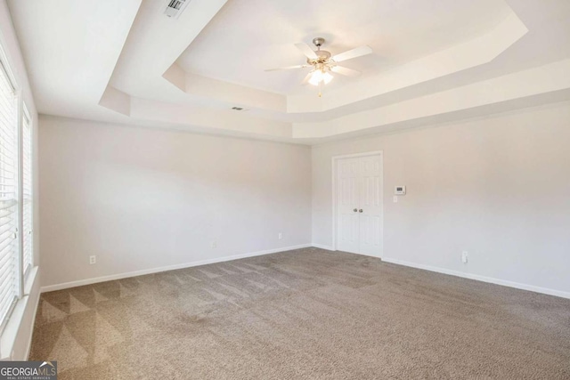 empty room with a raised ceiling, carpet flooring, and a healthy amount of sunlight