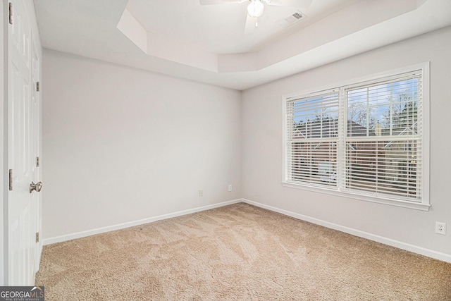 carpeted empty room featuring a raised ceiling and ceiling fan