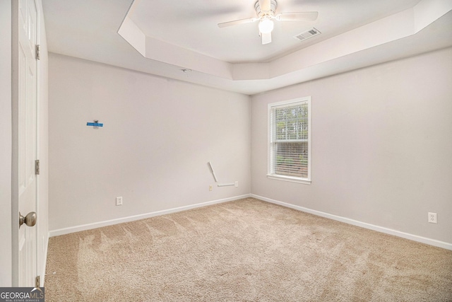 carpeted spare room with ceiling fan and a tray ceiling