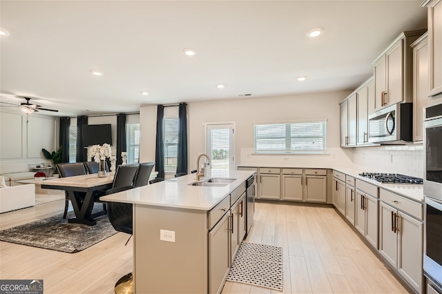 kitchen featuring stainless steel appliances, a kitchen island with sink, sink, tasteful backsplash, and ceiling fan