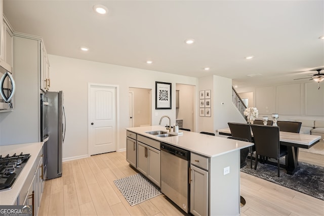 kitchen featuring a center island with sink, stainless steel appliances, light wood-style flooring, gray cabinetry, and a sink