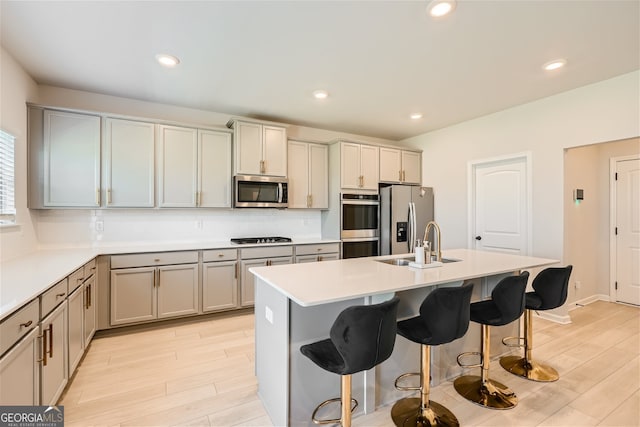 kitchen featuring light hardwood / wood-style flooring, tasteful backsplash, stainless steel appliances, a breakfast bar, and a kitchen island with sink