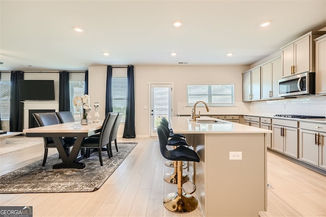 kitchen with gas cooktop, a sink, tasteful backsplash, stainless steel microwave, and an island with sink