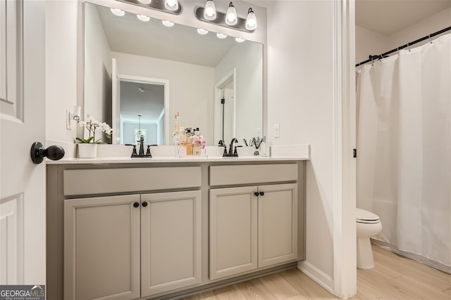 full bath with double vanity, a shower with shower curtain, toilet, wood finished floors, and a sink