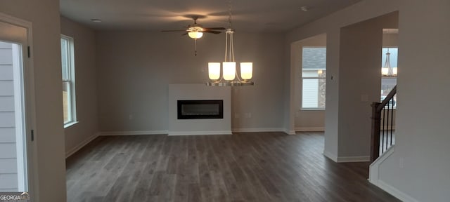 unfurnished living room featuring ceiling fan with notable chandelier and dark hardwood / wood-style flooring