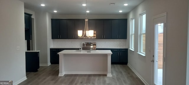 kitchen with hardwood / wood-style flooring, tasteful backsplash, sink, and an island with sink