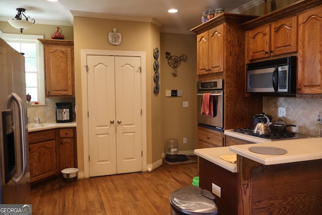 kitchen with decorative backsplash, light wood-type flooring, stainless steel appliances, and ornamental molding