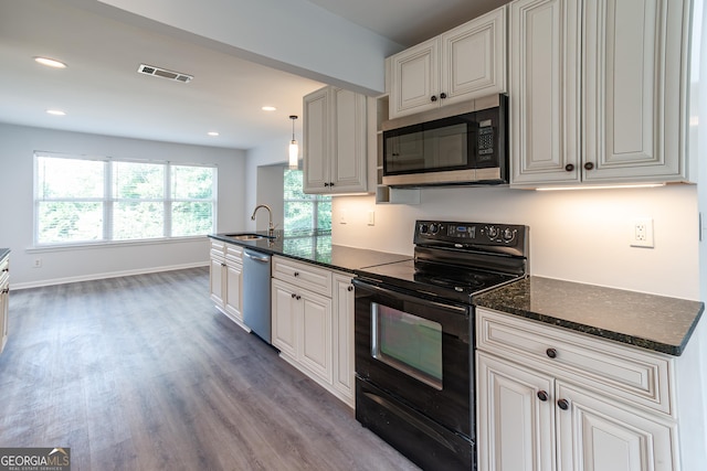 kitchen featuring appliances with stainless steel finishes, decorative light fixtures, wood-type flooring, sink, and dark stone counters