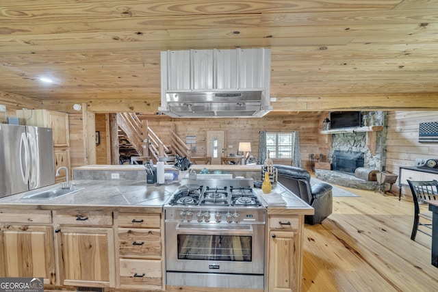 kitchen with light brown cabinetry, sink, stainless steel appliances, and wood walls