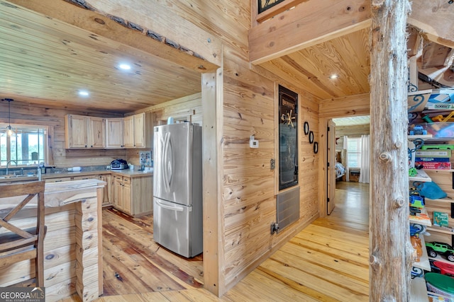 kitchen with wood walls, stainless steel fridge, light hardwood / wood-style floors, and light brown cabinets