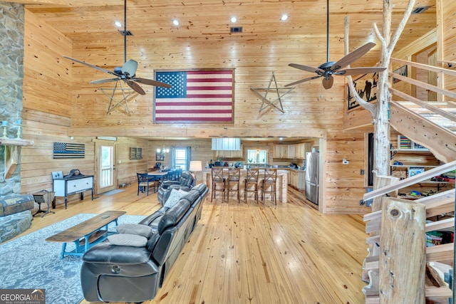 living room with wooden walls, light hardwood / wood-style flooring, and a towering ceiling