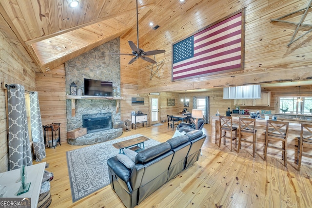 living room with a stone fireplace, wood walls, high vaulted ceiling, and wooden ceiling