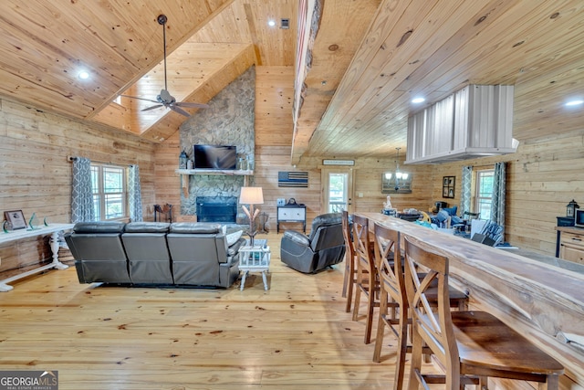 living room featuring wood walls, a stone fireplace, light hardwood / wood-style flooring, ceiling fan, and wood ceiling